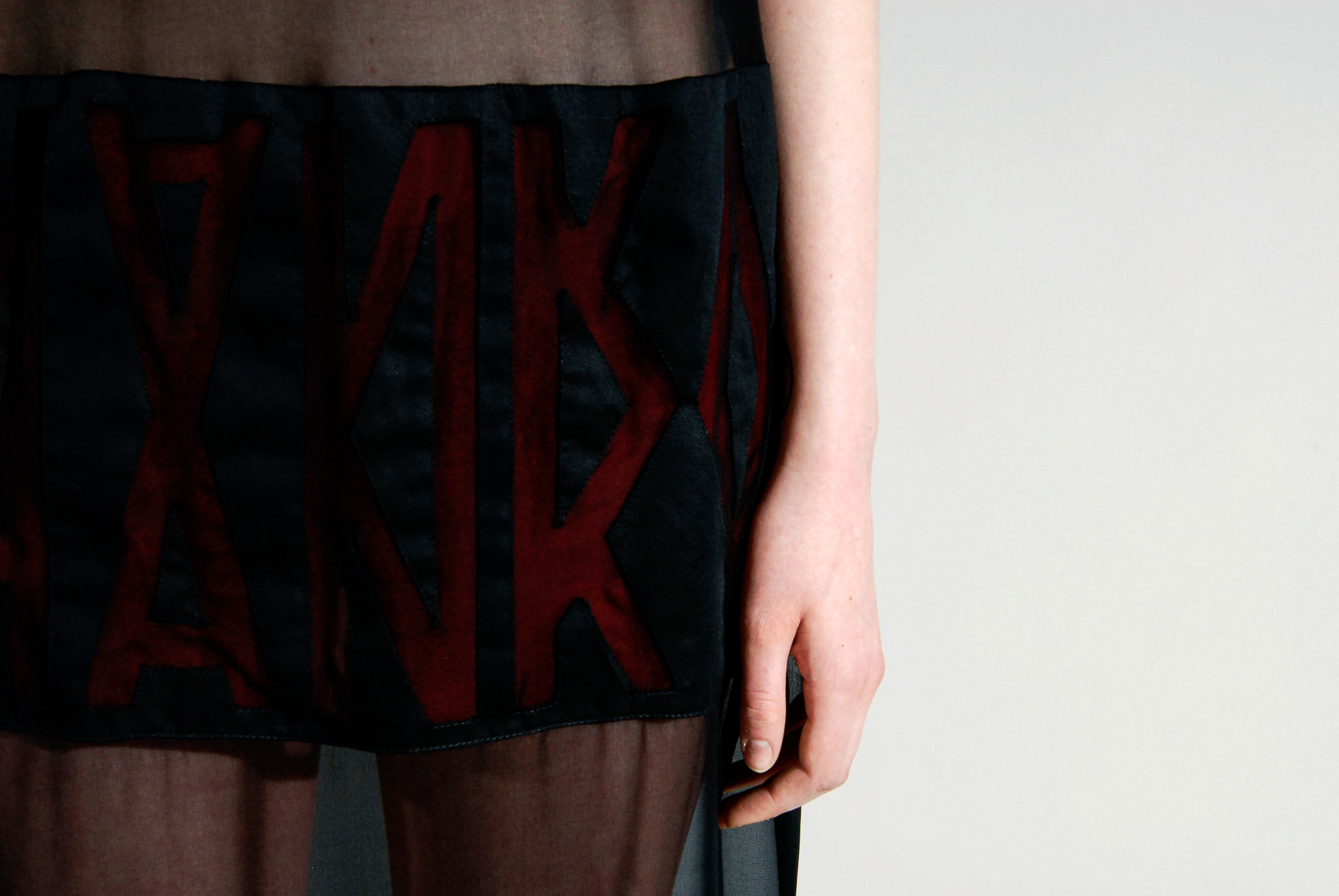 Close detail of lettering visible through the sheer black textile of Look 05.